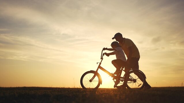 Happy family. dad teaches his son to ride bike. happy family kid dream concept. silhouette of a child riding a bicycle. silhouette of a father teaching his son to ride lifestyle a bicycle.