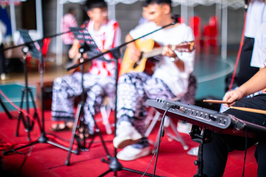 POV over Electronic Drum Kit and keyboard of a live acoustic music performance with guitarists, singers, and microphone.