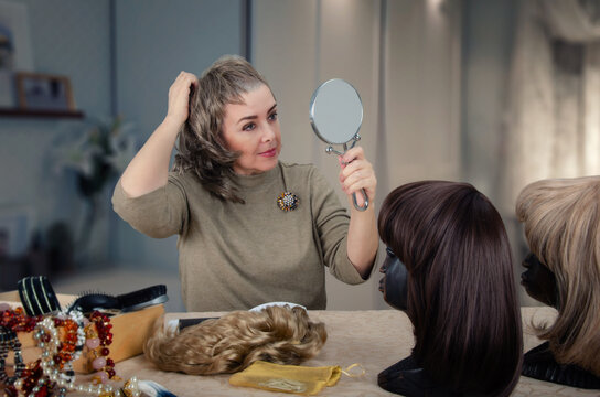 Mature cancer patient takes off her wig in a serene home environment, revealing her shaved head after chemotherapy.