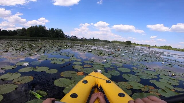 Kayaking along river through growing white lily nymph on sunny summer day. Person floating in boat on river with surface of water reflecting white clouds on calm day. Tourism. Active lifestyle. POV