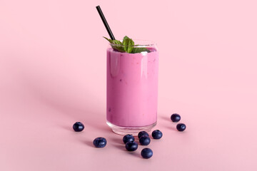 Glass of fresh blueberry smoothie with mint and berries on pink background