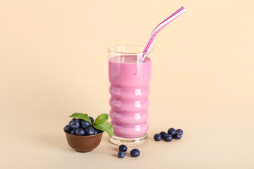 Glass of fresh blueberry smoothie and bowl with mint and berries on yellow background