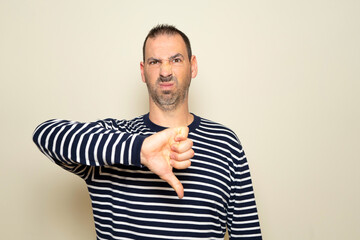 Bearded hispanic man about 40s wearing casual clothes looking unhappy and angry, showing rejection and negativity with thumbs down gesture. Bad expression.