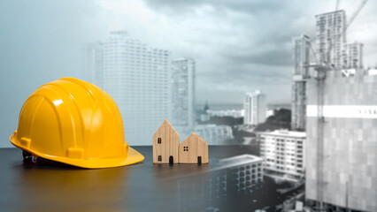 Hard hat and wooden house mockup placed at black tabletop on double exposure background of high...