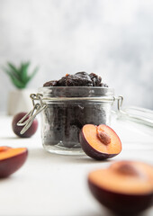 Dried sweet prunes in glass jar on light background with plum halves.Macro