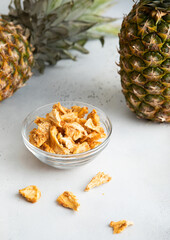 Dried pineapple slices chips in glass bowl on light background with ripe pineapple fruit.