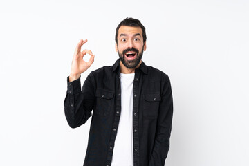 Young man with beard over isolated white background surprised and showing ok sign