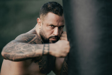 Boxer man with naked torso boxing outdoor. Brutal angry gang man lifestyle. Serious male sport. Strong muscular male body, muscles guy. Tattooed man boxing boxing bag. Power and sport.