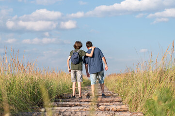 Teenager boy and his father walking in countryside, family summer outdoor trip