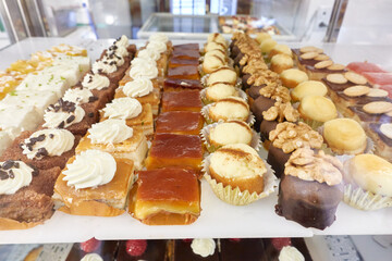 Display of cakes arranged in rows in the window of a bakery: tocinos de cielo, Spanish egg yolk flan, chocolate, cream