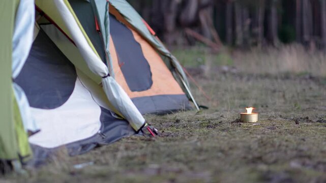 Mosquito repellent - citronella candle with flame near camping tents in forest. Lighted candle with lemongrass to prevent mosquito bites. Perfect for windless summer evenings outdoors.