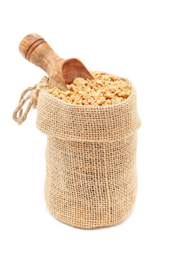 Close-up of Organic Soya Granules (Glycine max), in a jute bag with a scoop, Isolated on a white background.
