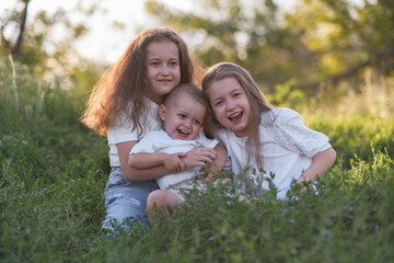 Three cheerful and happy children brouther and sisters are enjoying a playful and delightful moment in a sunlit grass field full of joy.