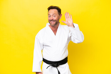 Middle age caucasian man doing karate isolated on yellow background saluting with hand with happy expression