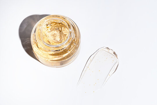 top view of glass jar and a smear of 24k gold cream gel for skin care on white background. Luxury cosmetics presentation.