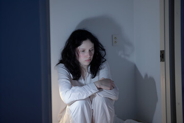 Young Woman Sitting on the Floor in a Dimly Lit Room, Contemplative Mood