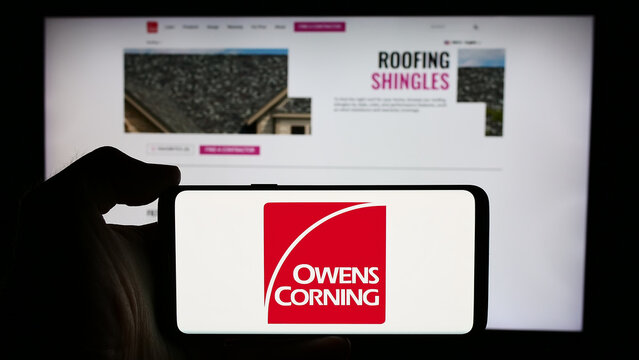 Stuttgart, Germany - 07-24-2024: Person holding cellphone with logo of US building materials company Owens Corning in front of business webpage. Focus on phone display.