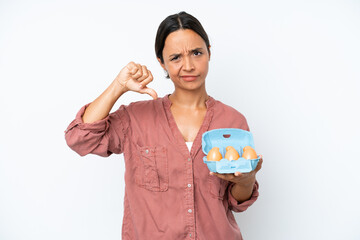 Young hispanic woman holding eggs isolated on white background showing thumb down with negative expression