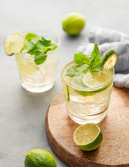 Two glasses lime mojito with mint and ice on a wooden board. Refreshing citrus cocktail on a light...