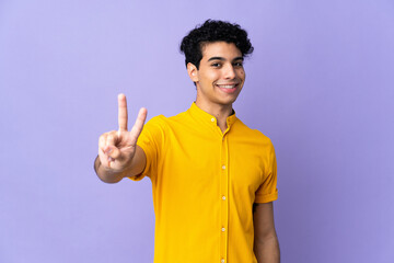 Young Venezuelan man isolated on purple background smiling and showing victory sign