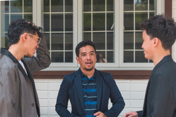 A short asian man talking with his two teenager sons. Having a lighthearted conversation. Wearing smart casual wear in front of their house.
