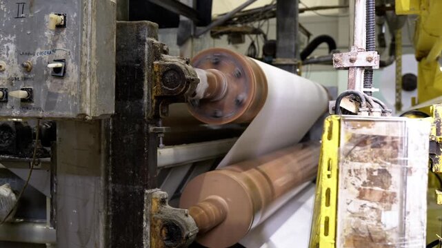 Drying wet paper sheet with hot mill machine in workshop closeup. Tissue pulp strip pressing with drying equipment at papermaking factory