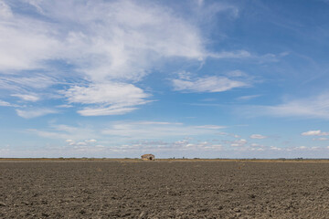 foto con aspecto de soledad y aislamiento de una finca rural Agricola en medio de un campo recién arado sin plantación y con un cielo azul con ligeras nubes blancas