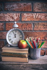 Back to school - clock, books and school supplies on bricks background