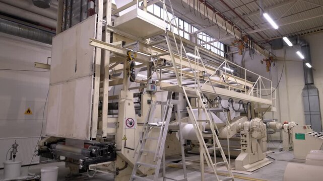 Service ground with metal ladder in papermaking plant workshop. Equipment of paper manufacturing and ready production rolls in warehouse