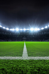 A large football stadium with lush green field is illuminated at night