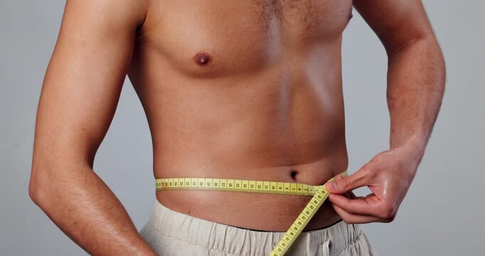 Man, topless and measuring tape on waist for results, fitness and weight loss with healthy diet on gray background. Male person, studio and wellness for exercise, progress and confidence with stomach