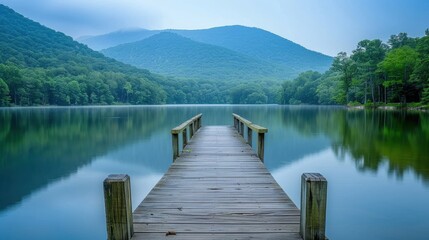 Serene lakeside dock extending over calm water, surrounded by lush green trees and mountains. Perfect for nature and landscape photography.