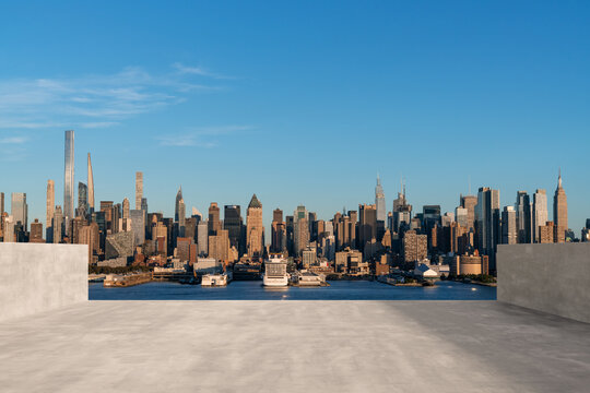 Concrete rooftop with a view of a city skyline across the river under a clear blue sky.