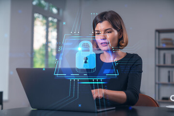 Woman working on laptop with cybersecurity hologram in office setting.