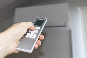 A person turns off, turns on, adjusts the air conditioner with a remote control. Unbearable heat. Harmfulness of air conditioners.