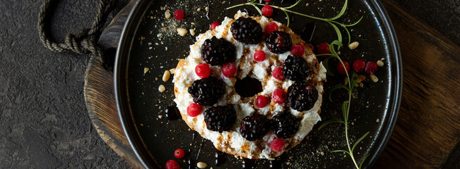 bagel with ricotta cheese and blackberries on a dark plate on a dark table, top view