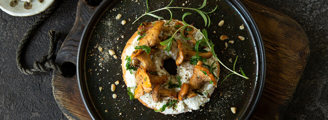 bagel with ricotta cheese and chanterelles on a dark plate on a dark table, top view