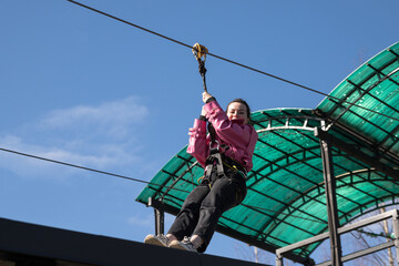 A happy young woman in casual clothes rides a zipline. The beginning of the descent on the zip...