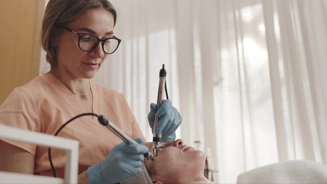 Beautician administers microcurrent treatment to a client in a salon for skin rejuvenation and therapy.