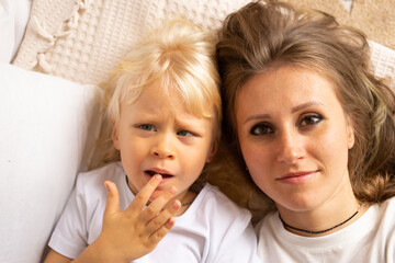 Mother and her little child baby boy lying on bed at home. Child boy with strabismus eyes, squinting eyes, cross-eye. Motherhood, affection