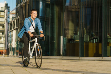 A man riding a bicycle past modern glass buildings, smiling in the warm sunlight, embodying urban commute.