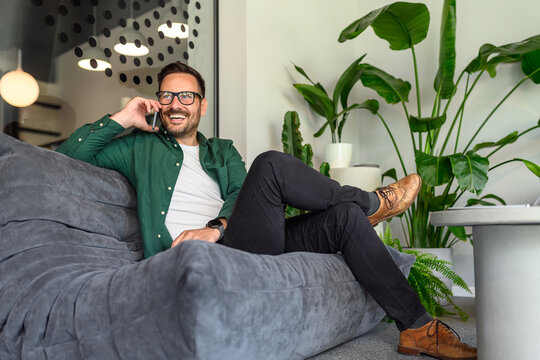 Low angle view of confident businessman discussing with client over mobile phone on sofa in office