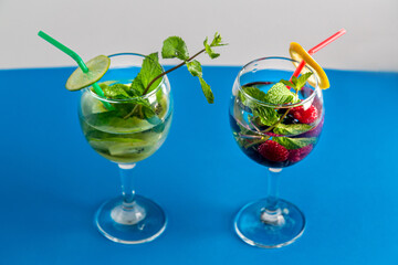 Two Glasses with fruit cocktail kiwi raspberry mint lime with ice on a blue background