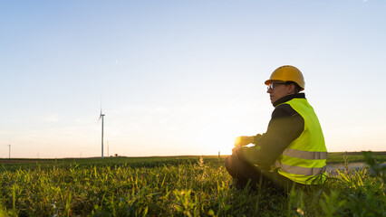 Worker sits on the grass and looks at wind turbines