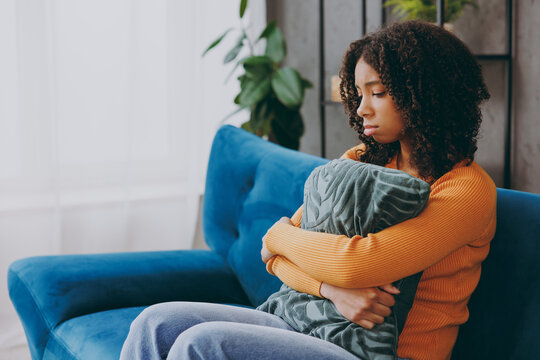 Side profile view little depressed upset sad kid teen girl wear casual clothes hold pillow sits on blue sofa couch stay at home hotel flat spend free spare time in living room indoor. Lounge concept.