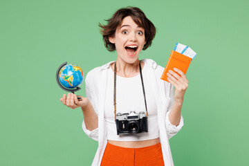 Traveler happy surprised shocked woman wear casual clothes hold passport ticket globe isolated on plain green background. Tourist travel abroad in free spare time rest getaway Air flight trip concept