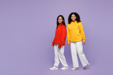 Full body side profile view two young little kid teen girls women they wear red yellow hoodie casual clothes walking go look camera isolated on plain pastel light purple background. Lifestyle concept.