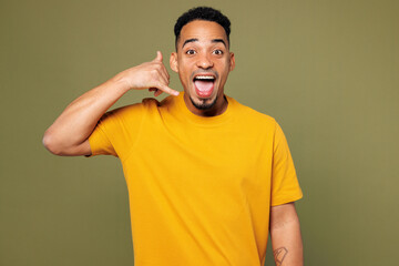 Young man of African American ethnicity he wears yellow t-shirt casual clothes doing phone gesture like says call me back isolated on plain pastel green background studio portrait. Lifestyle concept.