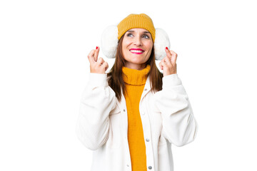 Middle age woman wearing winter muffs over isolated chroma key background with fingers crossing