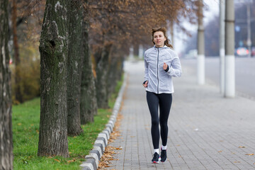 Woman Running Along Tree-Lined Pathway in Early Morning Fog